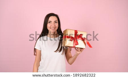 Young woman holding a smiling gift, on a pink background. High quality photo