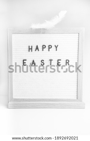 Easter greetings on a letterboard with text happy easter, with white feather
