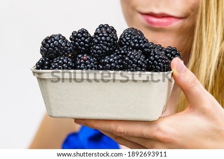 Girl holding fresh blackberry fruits in paper box. Healthy seasonal fruit, organic nutrition.