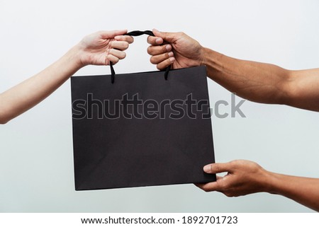 People hands holding giving black shopping paper bags over white background.