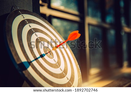 Dart arrow hit on bulleyes of dartboard to represent that the business reached the target  with dark tone picture style. Target and goal as concept. Royalty-Free Stock Photo #1892702746