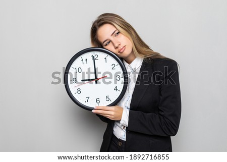 Portrait of beautiful young business woman holding in hands clock with sleepy mood on white background.
