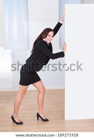 Full length of young businesswoman pushing blank billboard in office