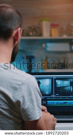Colorist working remotely overtime from home using editing software sitting in front of laptop late at night. Videographer processing audio film montage on professional in modern kitchen in midnight