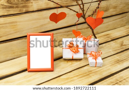 Planning until Valentine's Day photo frame on wooden background. White gifts are tied with a red ribbon. Branch with red hearts. Love background