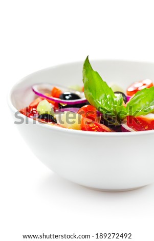 Light greek mediterranean salad with fresh vegetables, garnished with basil. White background. Selective focus - some vegetables are in focus, some are not. Vertical composition.