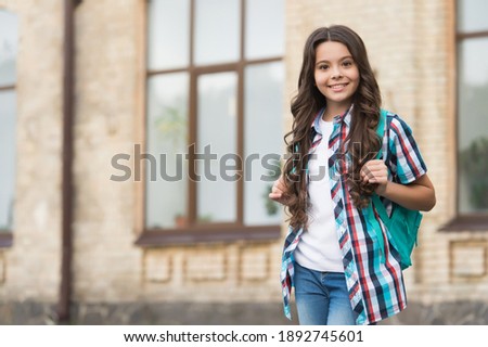 Happy kid with long wavy hair in casual fashion style carry travel bag urban outdoors, travelling, copy space.