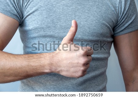 Happy young caucasian man in a gray t-shirt makes a thumb up sign showing close-up  . Language of the body. I like it. Well done. Promotion. Public relations.