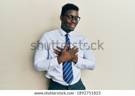 Handsome black man wearing glasses business shirt and tie smiling with hands on chest with closed eyes and grateful gesture on face. health concept. 