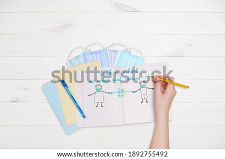 Child writing in the notebook.
Keeping social distance, wearing a surgical protective Medical mask for prevent virus Covid-19. Health care, medical, Education concept.
