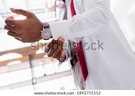 Cropped view of wristwatch on arm of african american businessman wearing white shirt on blurred background