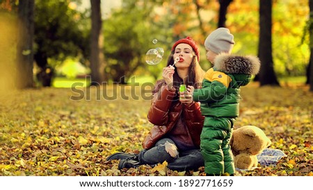 adult mother or nanny blows bubbles for a little boy. happy motherhood. cute kid playing in the park.