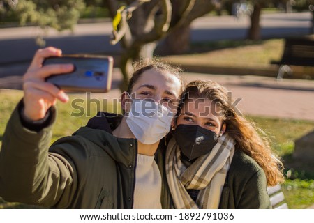 Young couple taking a selfie in the park with antivirus surgical mask
