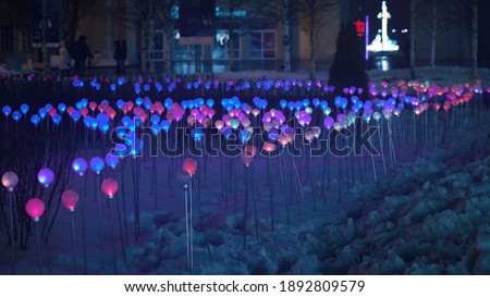Multicolored glowing glass balls on chrome sticks are stuck in the snow. Fluorescent lights play with light. Colors of rainbow. Flicker field. Festive decoration of parks and city. Depth of field.