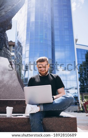 Young business man working on laptop and drinking coffee by the skyscraper