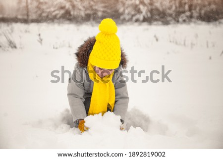 Baby girl plays with snow in nature in winter. Clothes in trendy colors. Ultimate grey and illuminating