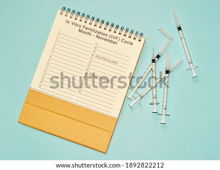 November IVF cycle calendar and disposable injection syringe on blue background