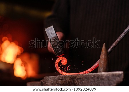 Blacksmithing. The blacksmith on the anvil measures the width of the split product and glowing sparks fly in all directions. Photo of red metal close-up.  Royalty-Free Stock Photo #1892824099