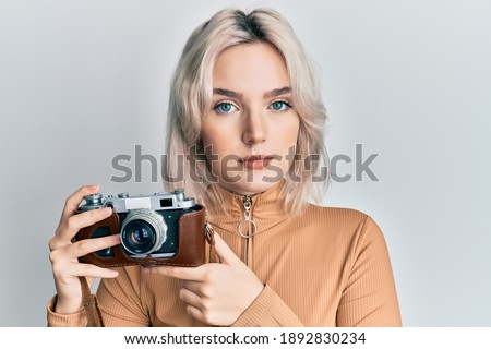 Young blonde girl holding vintage camera relaxed with serious expression on face. simple and natural looking at the camera. 
