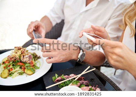 technology and people and concept - close up of couple with smatphones taking picture of food at restaurant terrace