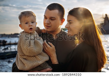 Happy caucasian Family: mom, dad and baby boy  at the quay. Parents looking at son and squinting at the sun. image with selective focus