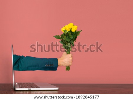 Hand coming out of a laptop with yellow roses in hand. Valentine's day Covid Concept. Royalty-Free Stock Photo #1892845177
