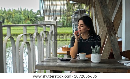 A young European girl sits at a table in a public place with a cup of coffee on a wooden table and looking on protective mask on a table