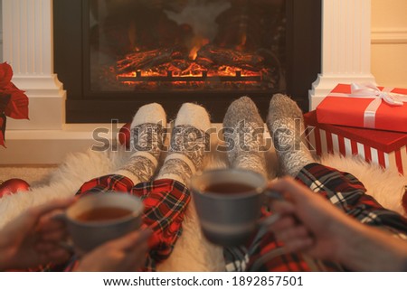 Couple with hot drinks resting near fireplace at home, closeup