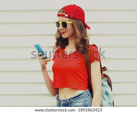 Portrait of happy woman with phone wearing a red baseball cap on a white background