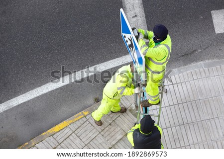 Workers installing a new road sign on street sidewalk. Public maintenance concept
