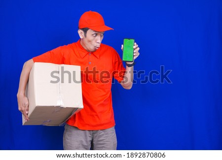Delivery Man Showing Phone Holding Box. Phone Green Screen. Delivery Boy Smiling. Man with Parcel in Hands isolated blue background