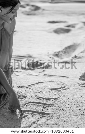 black and white image of a beautiful young african woman writing i love you on the sand with her finger