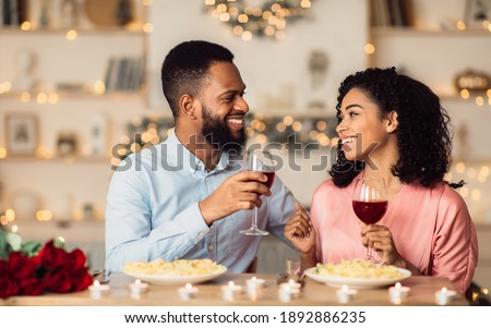 Handsome black man and pretty woman drinking wine at restaurant, toasting and celebrating Valentine's Day together. Couple of sweethearts having romantic dinner, enjoying festive meal in the evening Royalty-Free Stock Photo #1892886235