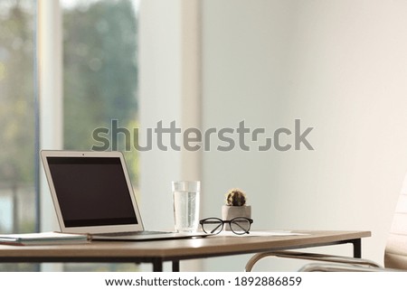 Modern laptop and glass of water on table in office. Space for text