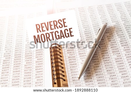Text reverse mortgage on paper card,pen, financial documentation on table - business, banking, finance and investment concept. close up of stock market chart.