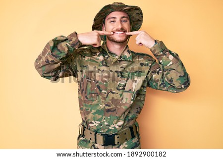 Young caucasian man wearing camouflage army uniform smiling cheerful showing and pointing with fingers teeth and mouth. dental health concept. 