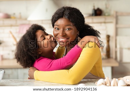 Happy Mother's Day Concept. Cute Little Black Girl Kissing And Embracing Her Happy Mom In Kitchen While They Cooking Together, Loving African Child Enjoying Spending Time With Mommy, Closeup