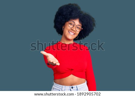 Young african american girl wearing casual clothes and glasses smiling cheerful offering palm hand giving assistance and acceptance. 
