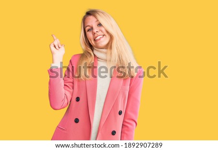 Young beautiful blonde woman wearing elegant clothes with a big smile on face, pointing with hand and finger to the side looking at the camera. 