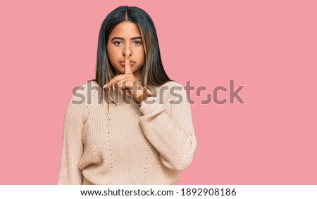 Young latin girl wearing wool winter sweater asking to be quiet with finger on lips. silence and secret concept. 