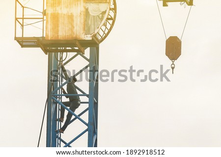 An Asian man crane operator climbs the crane ladder of the old hammerhead crane to the control cabin at a construction site. Focus on the crane.