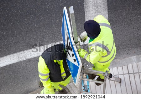 Workers changing a damaged road sign on street sidewalk. Winter time. Public maintenance concept