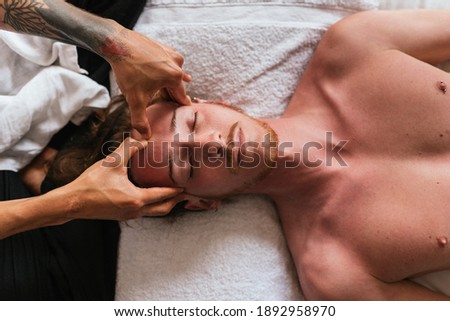 Stock photo of man enjoying face massage while lying in a towel.