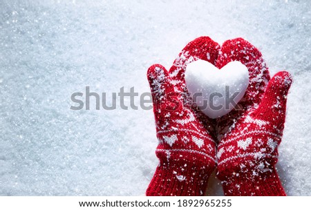 Female hands in knitted mittens with snowy heart against snow background. Love, winter and Valentines day romantic creative concept with copy space for text Royalty-Free Stock Photo #1892965255