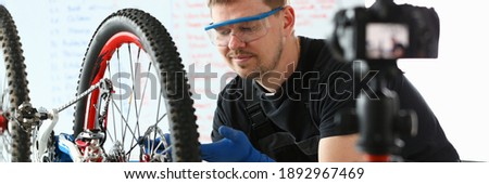 Cheerful guy in sportswear is looking at bike wheel upwards while camera is filming video