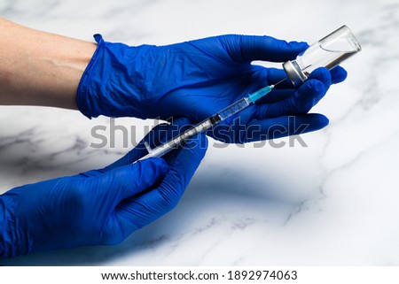 Hands in surgical gloves preparing Medical syringe and needle for hypodermic injection on a marble counter top.