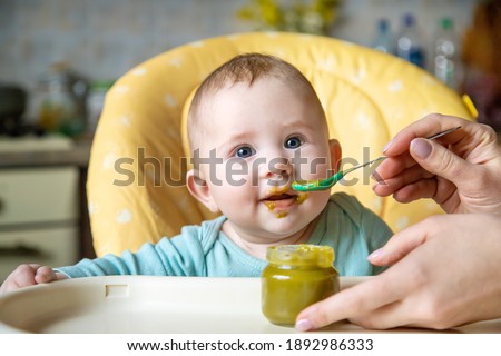 Little baby is eating broccoli vegetable puree. Selective focus. people. Royalty-Free Stock Photo #1892986333