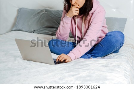 Beautiful young woman wearing casual jeans and shirt sitting on bed and using notebook. Freelance concept.