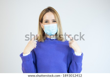 Woman wearing surgical mask pointing up fingers over white background.