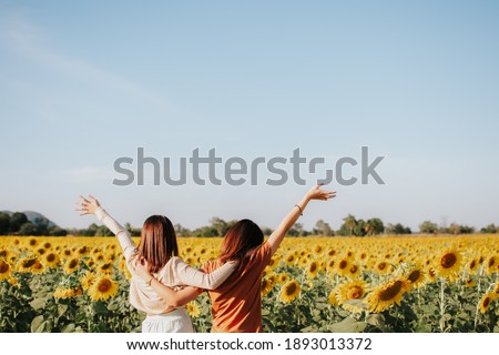 Two women are standing in a field of sunflower and hugging each other. Their hands are raised up to the sky. Friendship concept and copy space.
